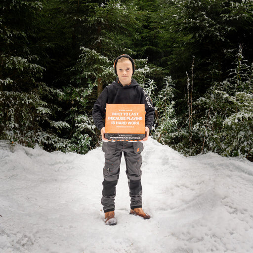 A boy in snow holds an orange box labeled "Built to Last Because Playing is Hard Work Workwear Bundle".